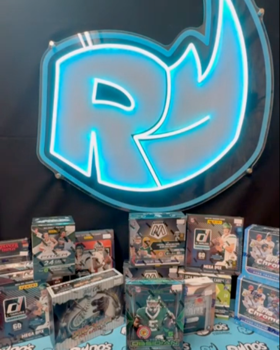Collection of sports trading card packs displayed in front of a neon sign